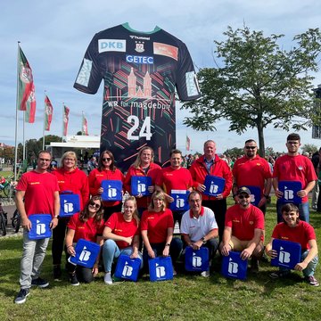 Eine Gruppe Menschen vom DLRG mit IB-Logos in der Hand vor einer Arena in Magdeburg