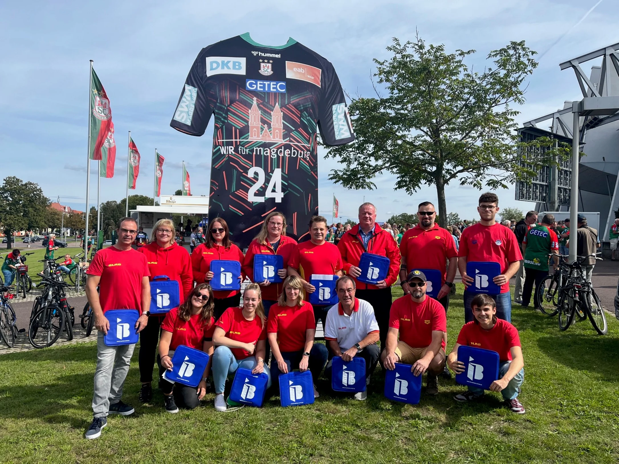 Eine Gruppe Menschen vom DLRG mit IB-Logos in der Hand vor einer Arena in Magdeburg