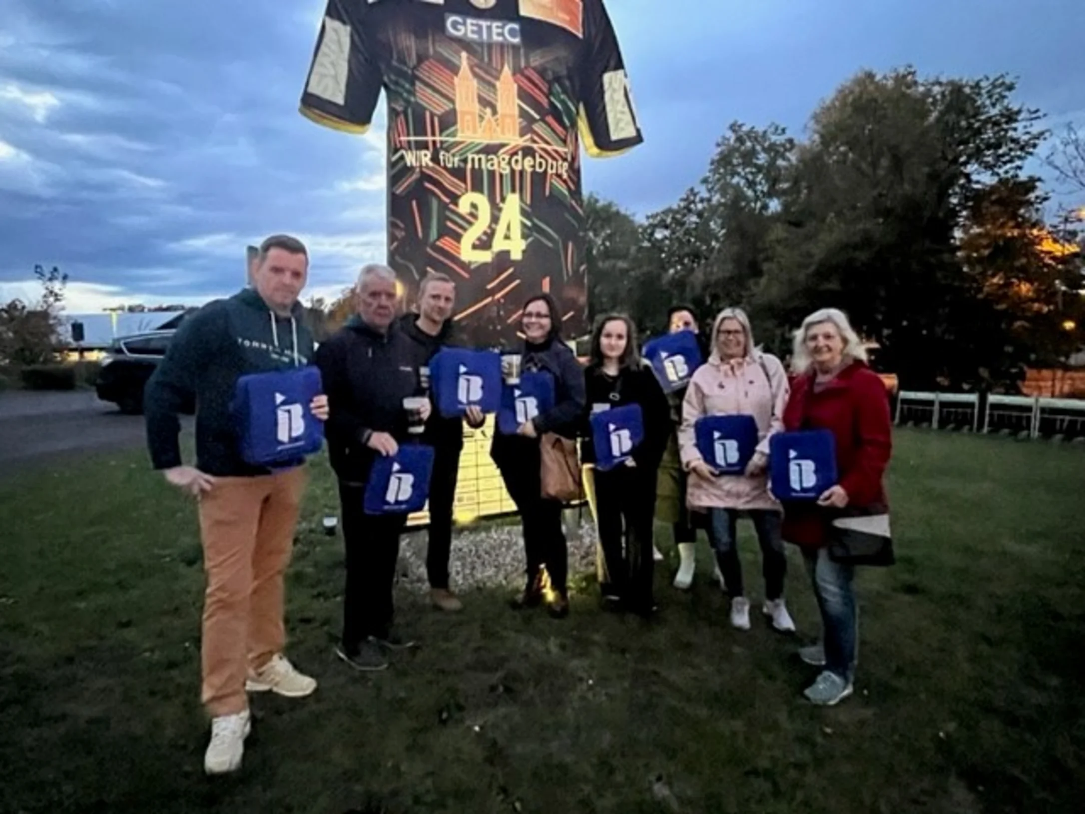 Vereinsmitglieder vom SV Eintracht Hohenwarthe mit IB-Logos in der Hand vor einer Arena in Magdeburg
