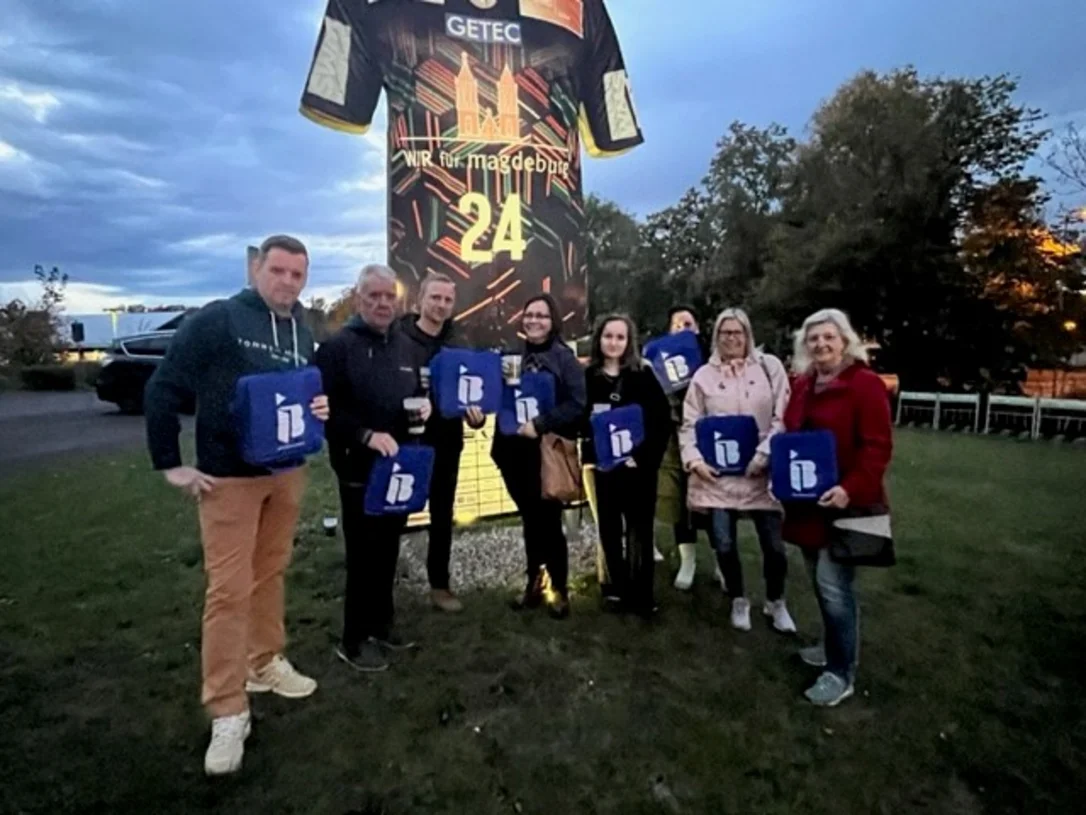 Vereinsmitglieder vom SV Eintracht Hohenwarthe mit IB-Logos in der Hand vor einer Arena in Magdeburg