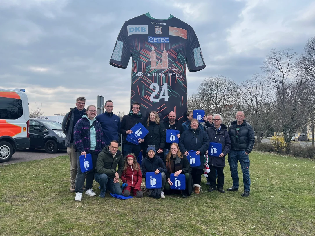 Mitglieder des THW Magdeburg mit IB-Logos in der Hand vor einer Arena in Magdeburg