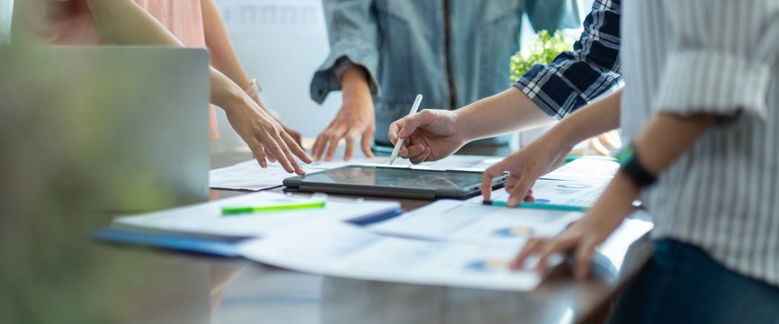 Menschen arbeiten zusammen an einem Tisch auf dem viele Unterlagen und ein Tablet liegen