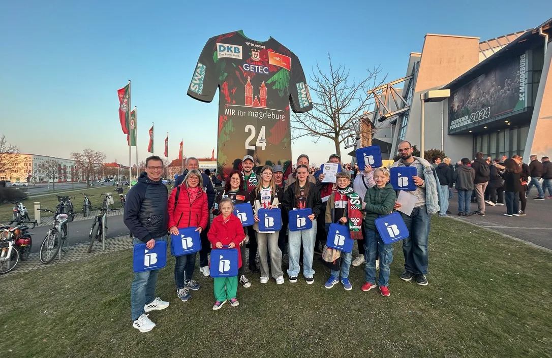 Mitglieder des Fördervereins Randau mit IB-Logos in der Hand vor einer Arena in Magdeburg