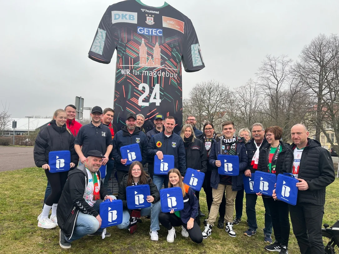 Mitglieder der freiwilligen Feuerwehr Jahrstedt mit IB-Logos in der Hand vor einer Arena in Magdeburg