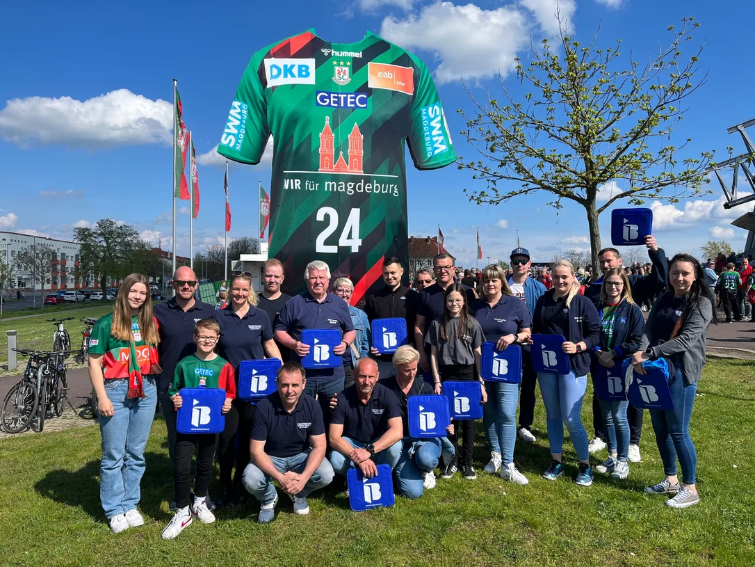 Mitglieder der freiwilligen Feuerwehr Preusslitz mit IB-Logos in der Hand vor einer Arena in Magdeburg
