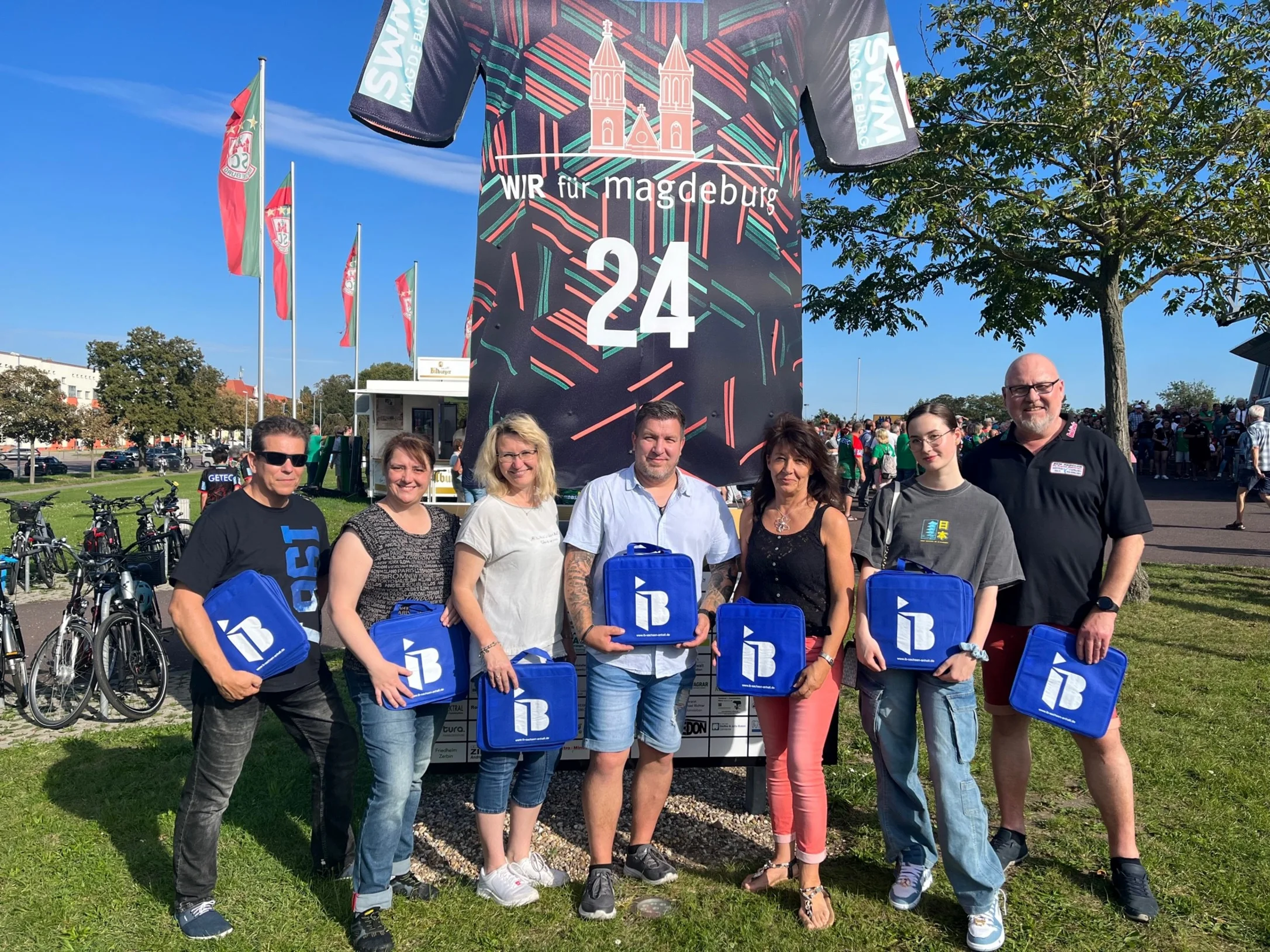 Ehrenamtliche der Psychosozialen Notfallversorgung des Landkreises Börde mit IB-Logos in der Hand vor einer Arena in Magdeburg