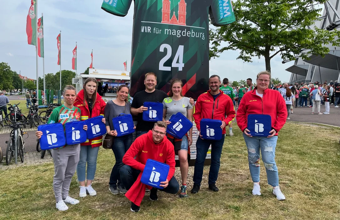 Mitglieder Arbeiter-Samariter-Bunds mit IB-Logos in der Hand vor einer Arena in Magdeburg