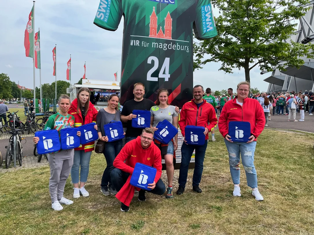 Mitglieder Arbeiter-Samariter-Bunds mit IB-Logos in der Hand vor einer Arena in Magdeburg
