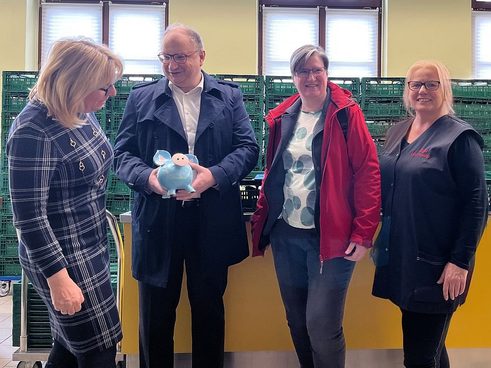 Auf dem Bild zu sehen sind ein Mann und drei Frauen. Der Mann hält ein Sparschwein in der Hand. 