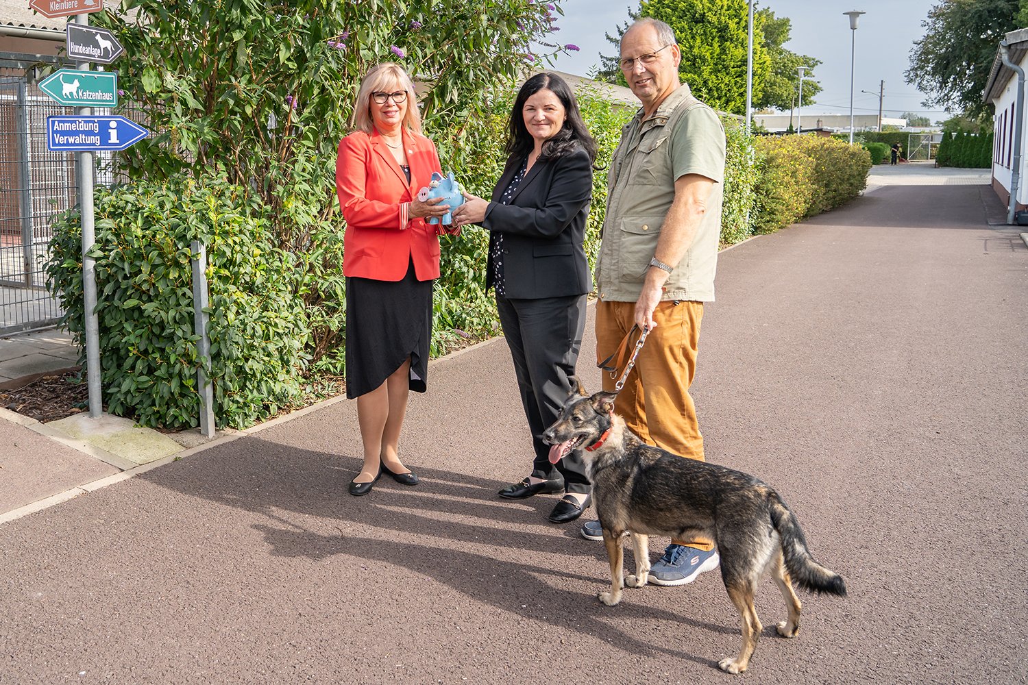 Auf dem Bild sind zu sehen: Simone Boris, Oberbürgermeisterin der Stadt Magdeburg, rechts daneben Mandy Schmidt, Vorstand der Investitionsbank Magdeburg  und Andreas Reichardt, Leiter des Tierheimes Magdeburg. Mandy Schmidt überreicht Simone Boris ein Sparschwein. Andreas Reichardt hält einen Hund an der Leine. 