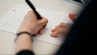 Eine Person schreibt Notizen auf ein Blatt Papier
