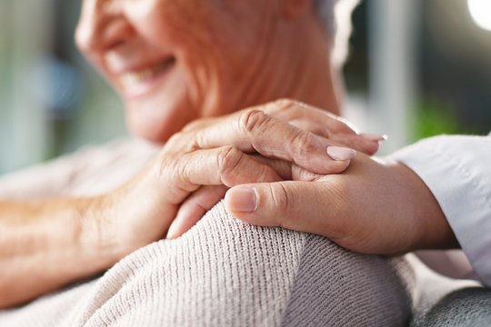 Die Hand einer jüngeren Person liegt auf der Schulter einer älteren Frau
