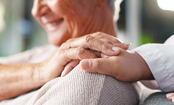 Die Hand einer jüngeren Person liegt auf der Schulter einer älteren Frau